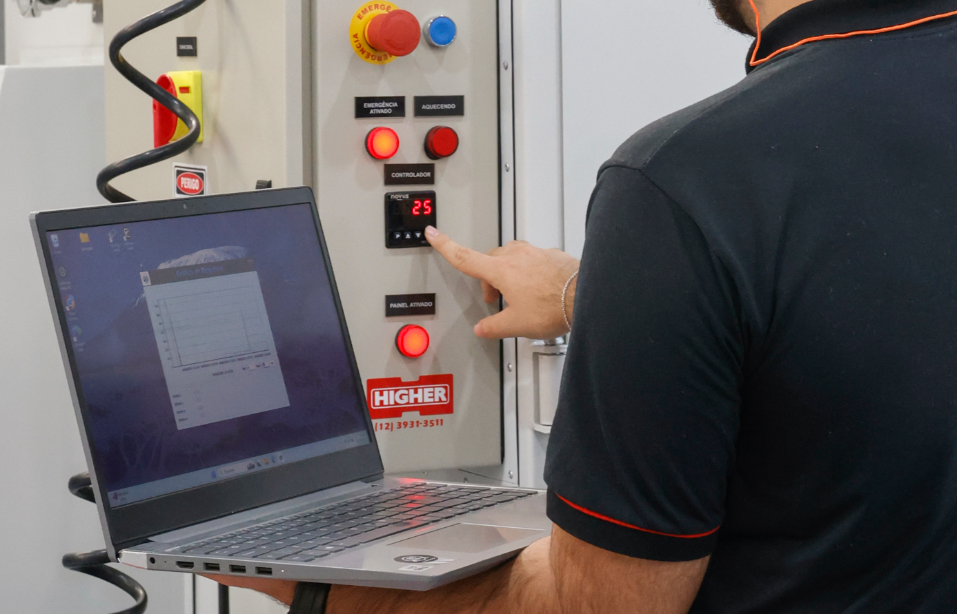 Colaborador da Higher com notebook em mãos ajustando o controlador de temperatura do painel elétrico